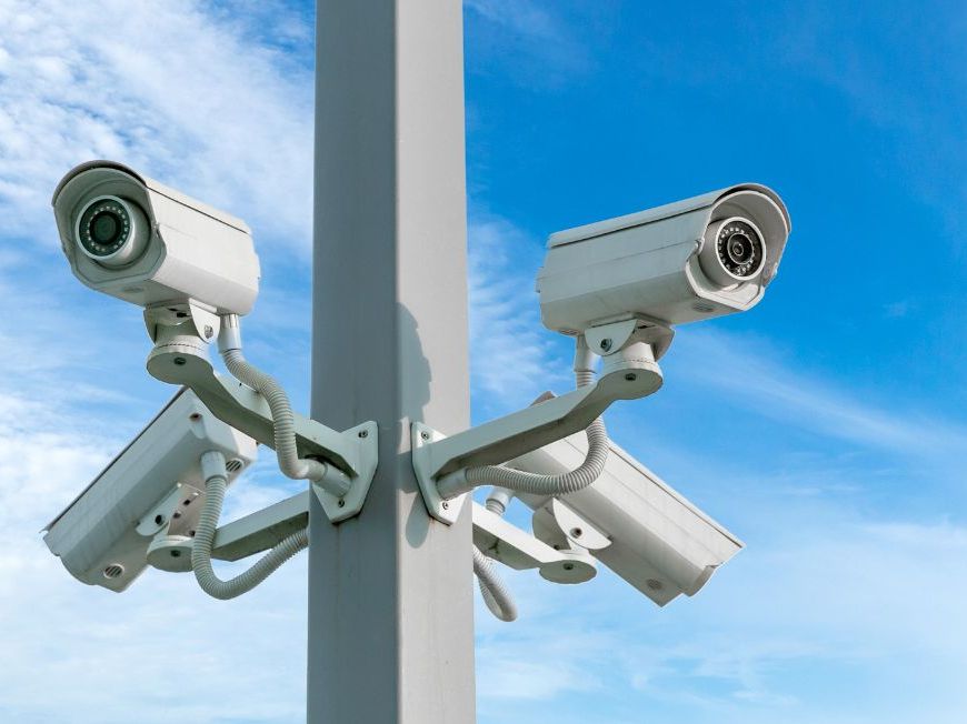 Four bullet security cameras mounted on a pole against a blue sky